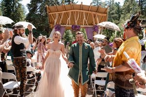 Wedding party celebrating outdoors with white chairs and natural forest backdrop.