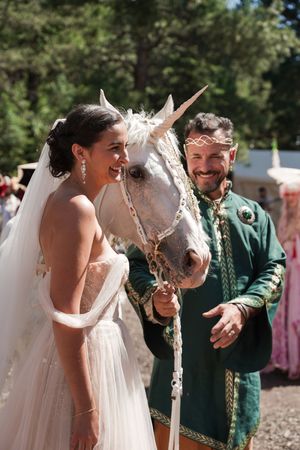 A unicorn joins the wedding celebration as guests gather around in a forest setting.