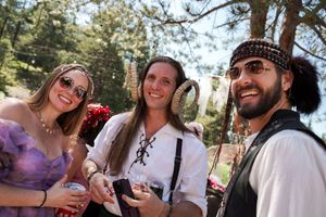 Festival attendees in period costumes socialize and laugh during an outdoor celebration.