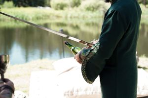 Person wearing dark clothing holding fishing gear by a calm lake.