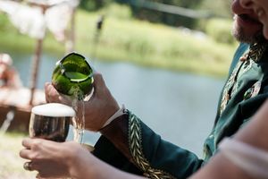 Hands pouring champagne into glasses at an outdoor party by a lake.