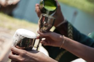 Close-up of hands pouring a green beverage into metallic cups outdoors.