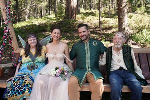 Wedding celebration attendees relaxing on wooden benches in a forest setting.