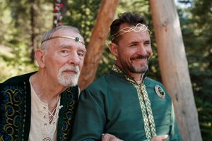 Two people in medieval-inspired clothing having a conversation in a wooded setting.