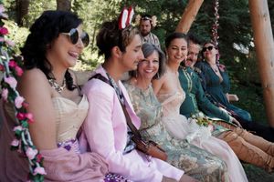 Wedding guests seated on rustic wooden benches decorated with pink and white floral arrangements.