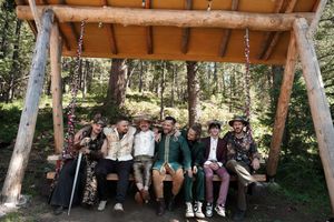 Wedding guests seated under wooden pavilion in forest setting during ceremony.