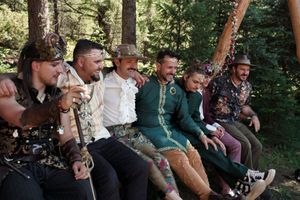 Group of wedding guests laugh together during outdoor forest celebration.