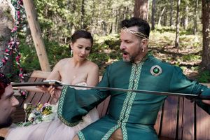Wedding party members seated on rustic wooden benches in a forest clearing.