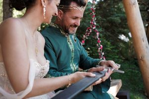 A couple dressed in wedding attire sits together on a wooden bench with floral decorations.