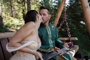 Wedding couple shares intimate moment in forest setting with decorative backdrop.