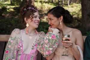 Two people in elegant attire share a laugh while enjoying drinks at an outdoor celebration.