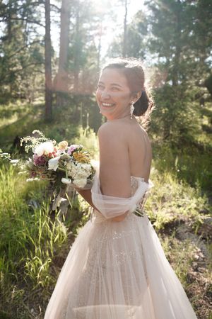 Elegant white wedding dress with floral bouquet captured in golden sunlit forest.