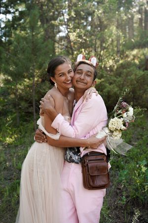 Two people embrace outdoors in a sunlit forest setting during a wedding celebration.