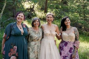 A group of friends pose together in elegant dresses at an outdoor wedding celebration.