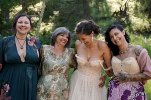 Four friends share a joyful moment together at an outdoor wedding celebration.