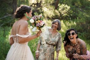 Wedding attendees laugh together during a candid moment in a forest setting.