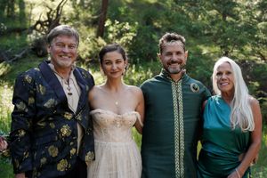 Wedding party poses together outdoors wearing elegant attire in a forest setting.