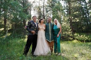 A wedding party poses casually in a wooded outdoor setting with trees and natural sunlight.
