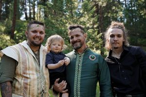 Group gathered outdoors at forest wedding with one wearing an ornate green embroidered jacket.