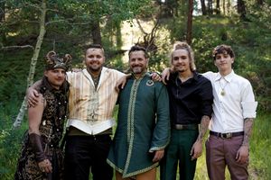 Wedding party members gather in a forested area wearing coordinated green and formal attire.