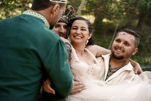 A group shares a candid laughing moment in formal wedding attire against a woodland backdrop.