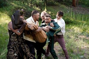 Wedding party members playfully carry someone in a candid outdoor group photo.