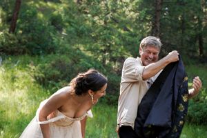A couple shares a joyful candid moment in a sunlit forest clearing at a wedding celebration.
