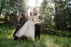 Wedding party taking celebratory photos in a sun-dappled forest clearing.