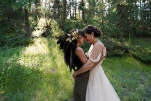 Two people share an intimate moment in wedding attire surrounded by sunlit forest scenery.