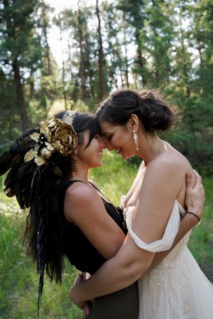 A tender embrace between two people in wedding attire with one wearing a dramatic floral headdress.
