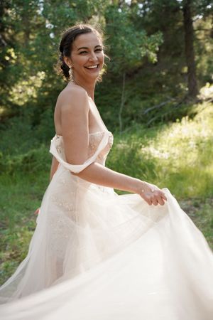 A flowing white wedding gown twirls gracefully in a sunlit forest setting.
