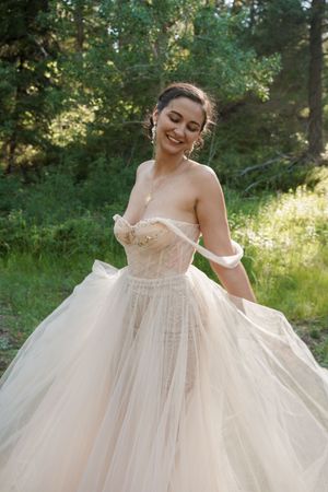 A stunning wedding dress with a tulle ballgown skirt and strapless corset bodice in a sunlit forest setting.