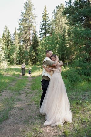 A couple shares a romantic dance moment on a forest path surrounded by tall evergreen trees.