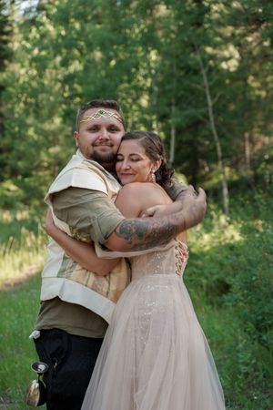 Couple embraces in woodland setting during rustic outdoor wedding ceremony.