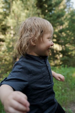 A young child with blonde wavy hair smiles while playing outdoors in a black shirt.