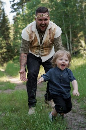 Playful moment between adult in medieval costume and young child running on forest trail.
