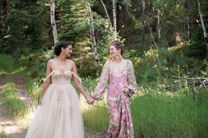 A couple walking hand in hand through a sunlit forest path wearing beautiful gowns.