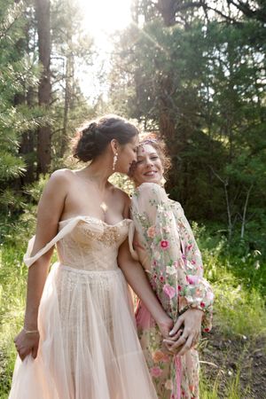 A heartwarming outdoor wedding scene shows tender embraces against a backdrop of sunlit trees.