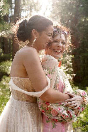 Two people share a joyful embrace in a sunlit forest clearing with soft golden backlighting.