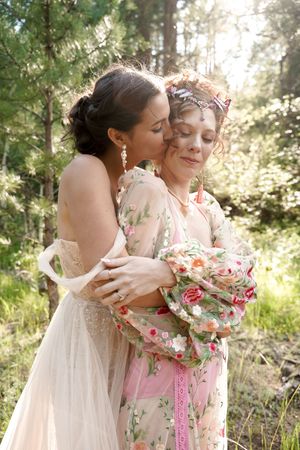 A tender moment captured between two people in floral and white dresses against a forest backdrop.