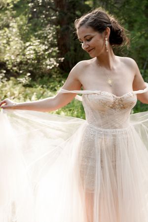 Ethereal wedding dress with delicate lace detail and flowing tulle skirt in natural outdoor setting.
