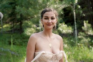 Bride in strapless lace wedding dress smiles in sunlit woodland clearing.