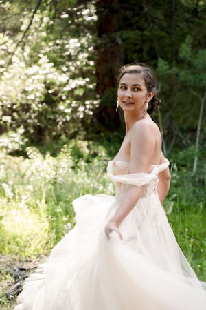 A flowing white wedding dress twirls gracefully in a sunlit forest setting.