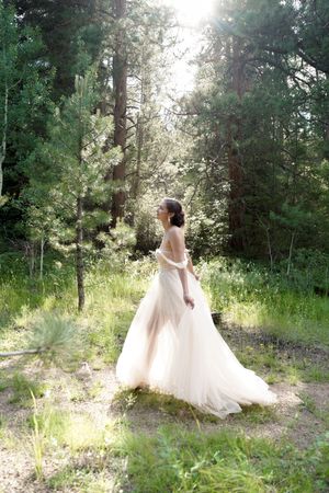 Ethereal bridal portrait showing flowing dress in backlit forest setting.