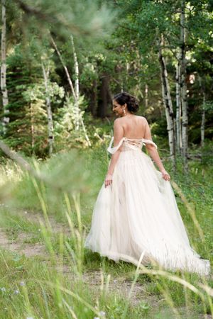 A person in a flowing white wedding dress poses elegantly in a serene forest setting.