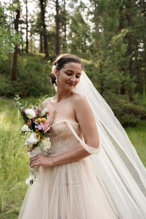 Elegant bridal portrait with white bouquet in a serene forest setting.