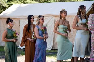 Wedding guests in colorful formal dresses stand in a line near a tent outdoors.