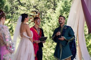 A wedding ceremony under a decorated arch in a forest with medieval-themed attire and decor.