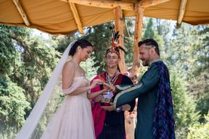 Celebratory scene beneath a tan canopy during a woodland wedding ceremony with floral decorations.