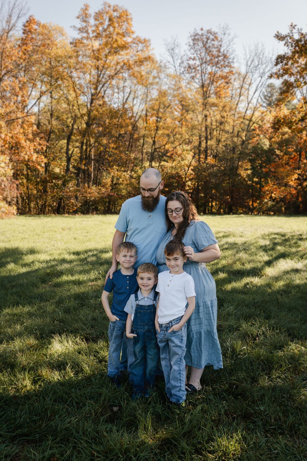 A group poses together on a grassy hillside surrounded by fall foliage.